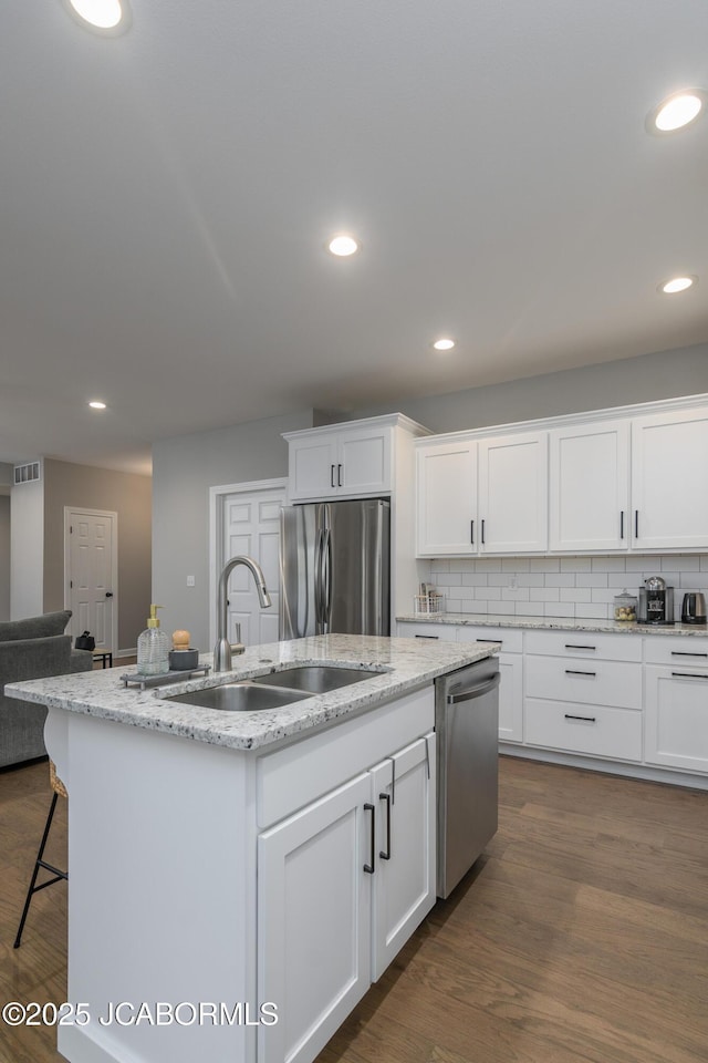 kitchen featuring tasteful backsplash, a center island with sink, dark wood finished floors, appliances with stainless steel finishes, and a sink