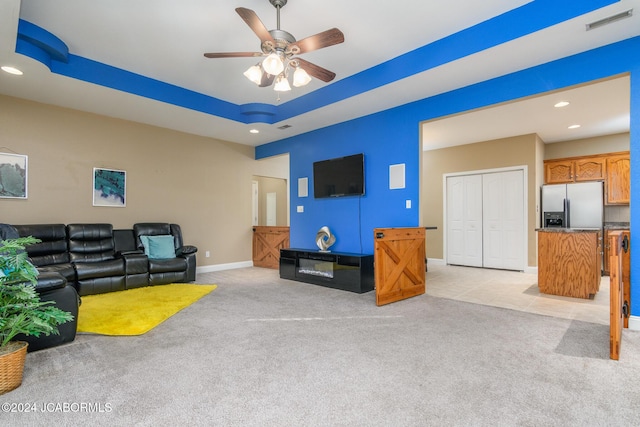 living room featuring ceiling fan, a raised ceiling, and light carpet