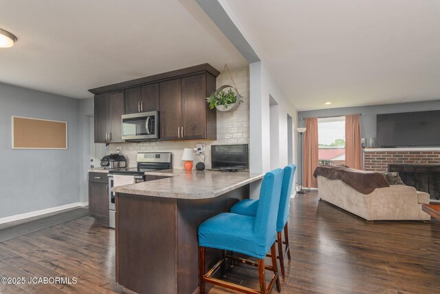 202 S Fourth St, Linn, MO 65051 - kitchen featuring a breakfast bar area, dark brown cabinets, dark wood-type flooring, backsplash, and appliances with stainless steel finishes