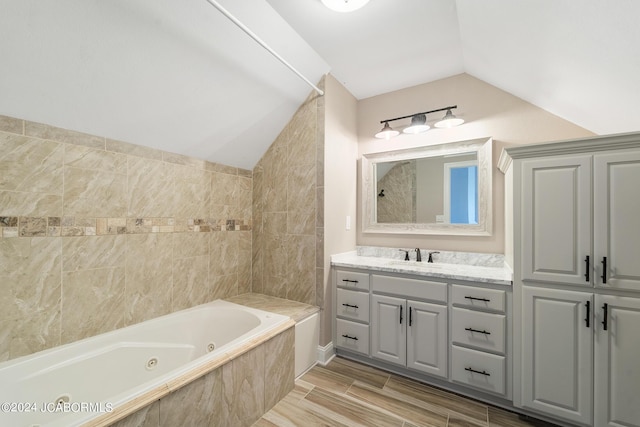 bathroom featuring a relaxing tiled tub, lofted ceiling, and vanity