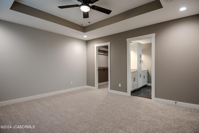 unfurnished bedroom featuring a walk in closet, baseboards, a tray ceiling, recessed lighting, and dark colored carpet