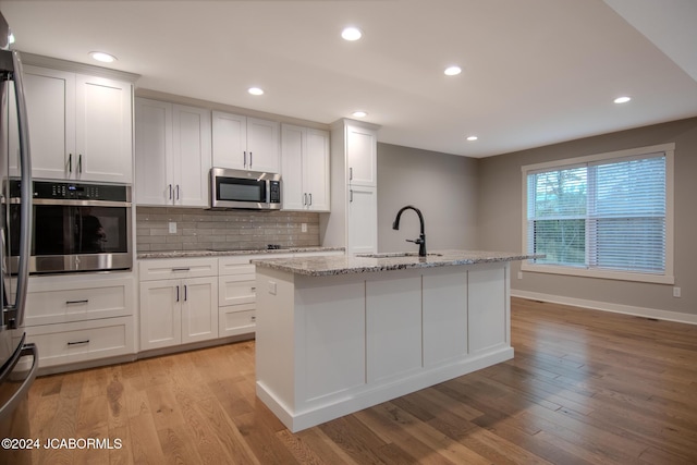 kitchen featuring a sink, light wood-type flooring, tasteful backsplash, and appliances with stainless steel finishes