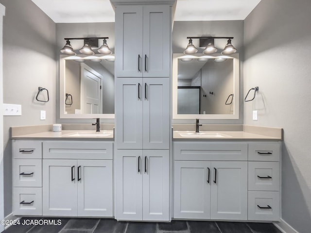 bathroom featuring double vanity, a shower with door, baseboards, and a sink