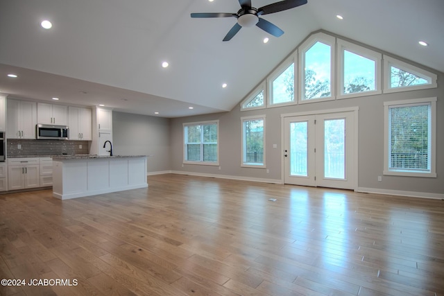 unfurnished living room with recessed lighting, light wood-style floors, baseboards, and high vaulted ceiling