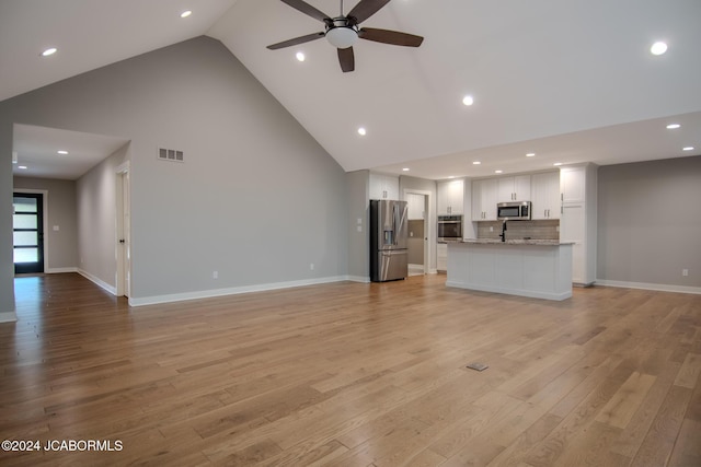 unfurnished living room with light wood finished floors, visible vents, baseboards, high vaulted ceiling, and a ceiling fan