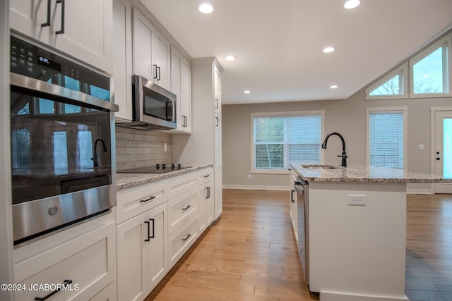 kitchen with a center island with sink, a sink, decorative backsplash, light wood-style floors, and appliances with stainless steel finishes