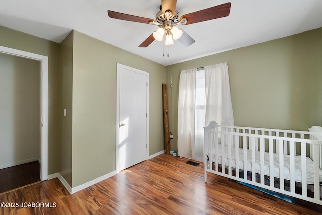 unfurnished bedroom featuring a nursery area, ceiling fan, and hardwood / wood-style floors