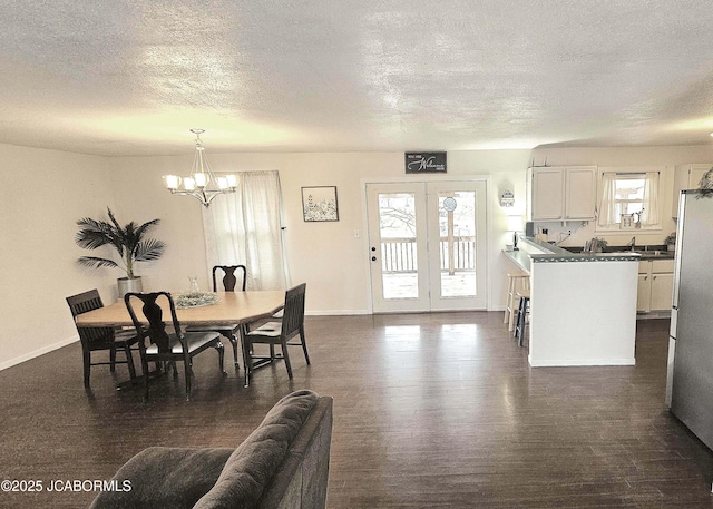 dining area with dark wood-type flooring, french doors, a textured ceiling, and a notable chandelier