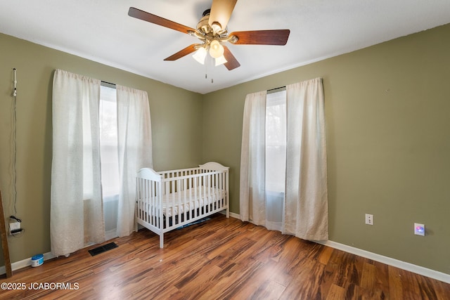 unfurnished bedroom featuring dark hardwood / wood-style flooring, a crib, and ceiling fan