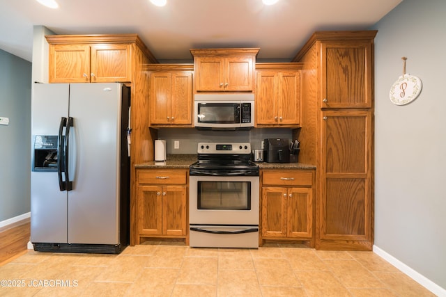 kitchen with brown cabinetry, baseboards, stainless steel appliances, and dark stone counters