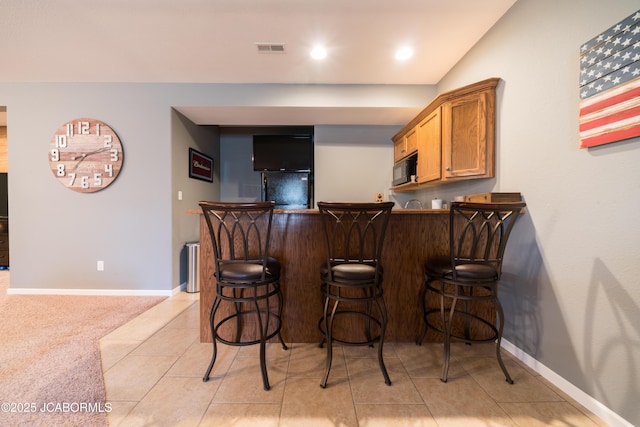 bar featuring baseboards, visible vents, black appliances, bar area, and light colored carpet