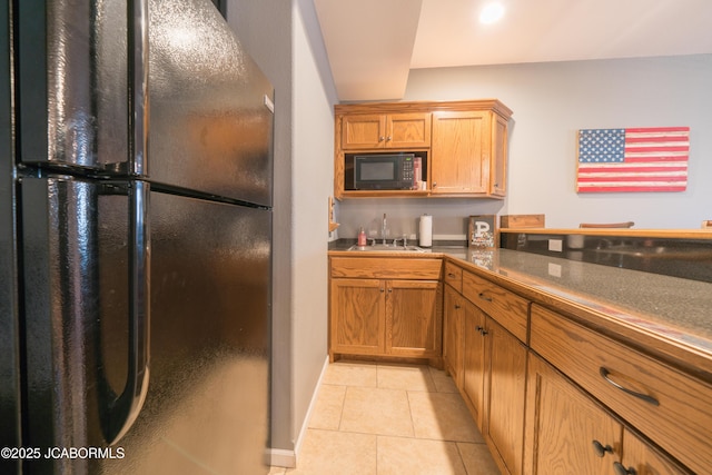 kitchen with brown cabinets, black appliances, a sink, dark countertops, and light tile patterned floors