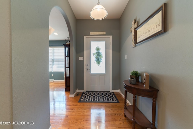 entrance foyer featuring baseboards, arched walkways, and light wood-type flooring