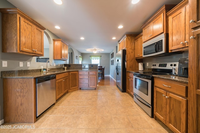 kitchen featuring recessed lighting, appliances with stainless steel finishes, a peninsula, arched walkways, and brown cabinetry