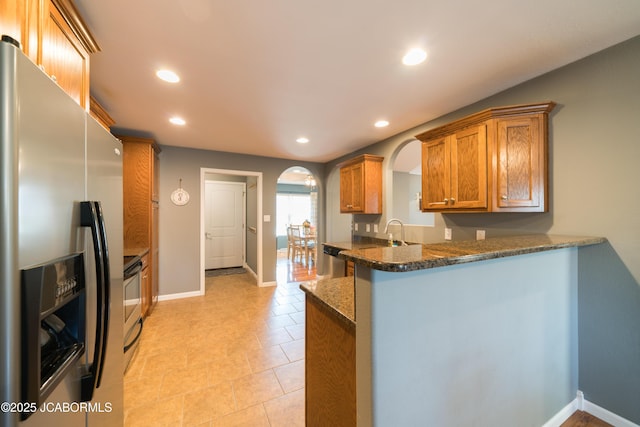 kitchen with recessed lighting, brown cabinetry, arched walkways, and appliances with stainless steel finishes