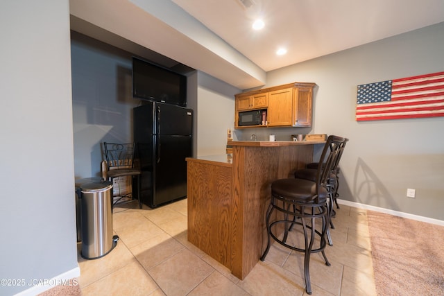 kitchen featuring black appliances, a kitchen breakfast bar, a peninsula, brown cabinetry, and baseboards