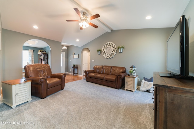 living room with a ceiling fan, baseboards, vaulted ceiling with beams, arched walkways, and light carpet