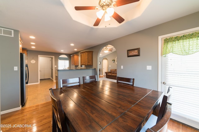 dining area with a ceiling fan, light wood-style flooring, recessed lighting, arched walkways, and a raised ceiling