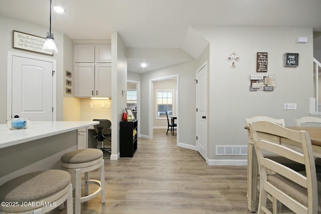 kitchen featuring decorative light fixtures, built in desk, white cabinets, and light wood-type flooring