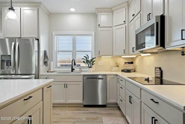 kitchen featuring sink, hanging light fixtures, stainless steel appliances, light hardwood / wood-style floors, and white cabinets