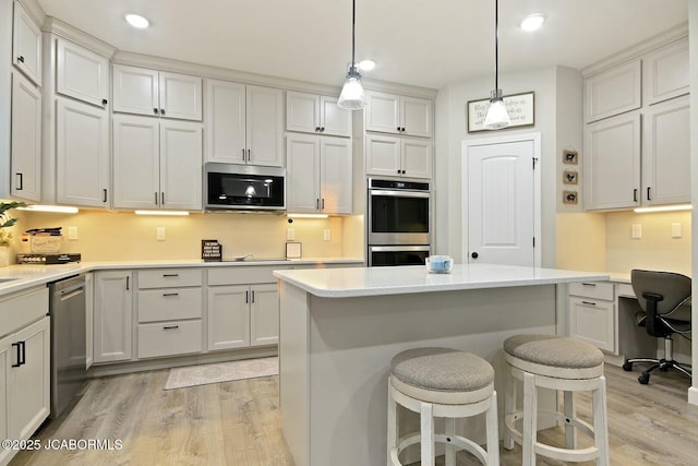 kitchen with light hardwood / wood-style flooring, a breakfast bar, appliances with stainless steel finishes, hanging light fixtures, and a kitchen island