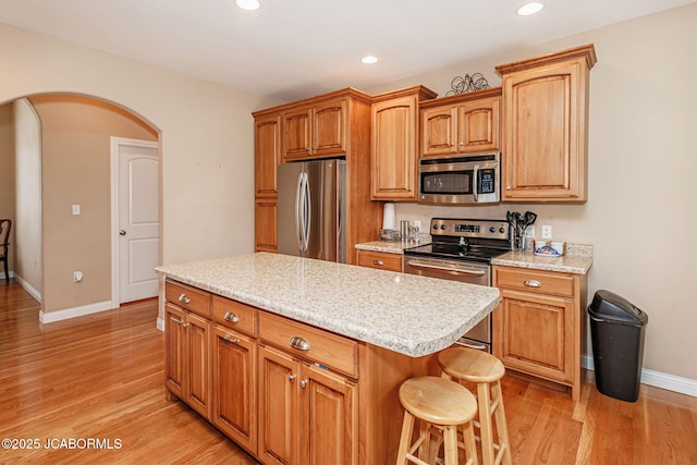 2414 Camzie Dr, Jefferson City, MO 65101 - kitchen with baseboards, light wood-style flooring, a breakfast bar area, appliances with stainless steel finishes, and arched walkways