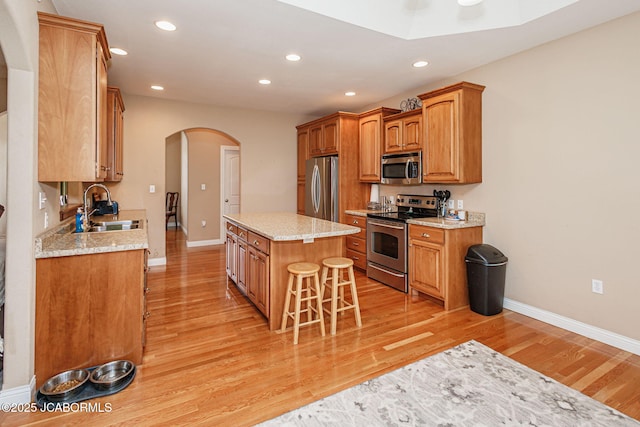2414 Camzie Dr, Jefferson City, MO 65101 - kitchen featuring light wood-style flooring, a kitchen island, appliances with stainless steel finishes, arched walkways, and a sink