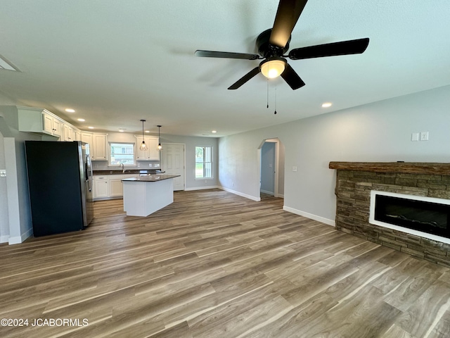 unfurnished living room with light hardwood / wood-style floors, a stone fireplace, ceiling fan, and sink