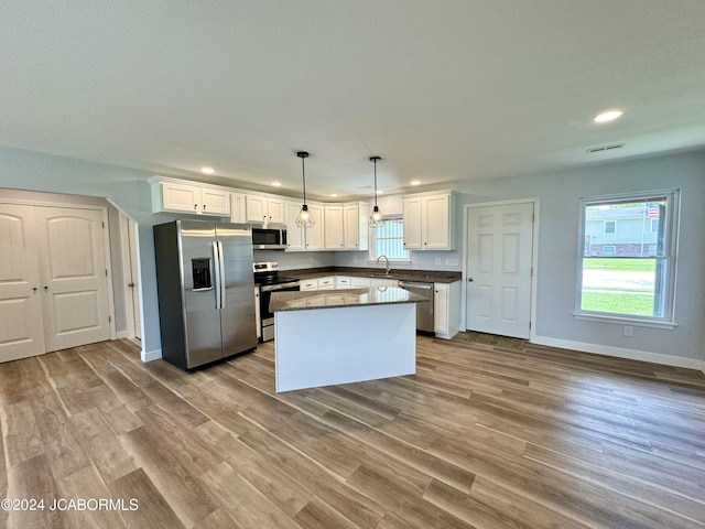 kitchen with white cabinets, light hardwood / wood-style floors, decorative light fixtures, and appliances with stainless steel finishes