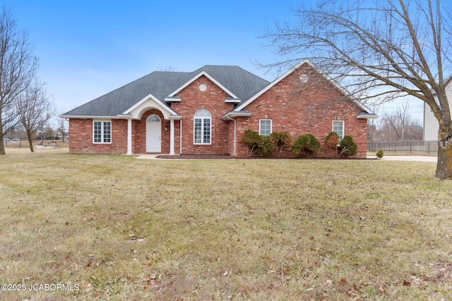 view of front of house featuring roof with shingles, a front yard, fence, and brick siding