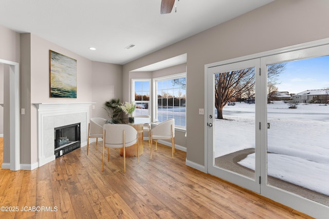living area with visible vents, baseboards, a tiled fireplace, ceiling fan, and light wood finished floors