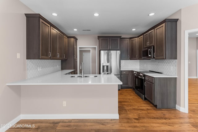 kitchen with baseboards, dark brown cabinetry, a peninsula, stainless steel appliances, and light wood-style flooring