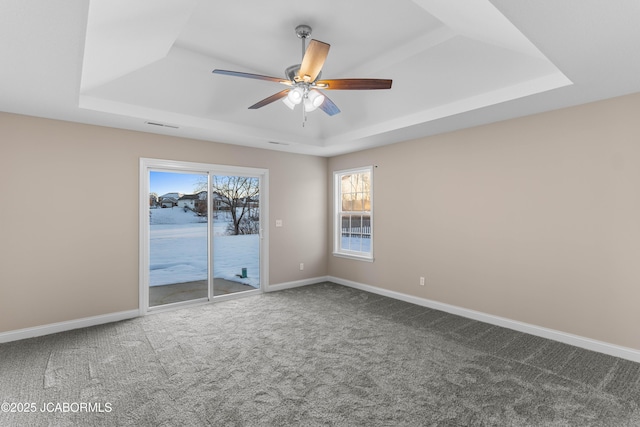 carpeted spare room featuring visible vents, baseboards, a raised ceiling, and a ceiling fan