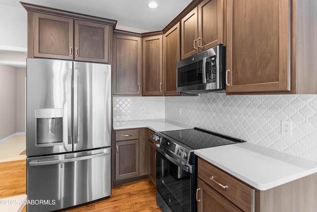kitchen with stainless steel appliances, light wood-style flooring, light countertops, and decorative backsplash