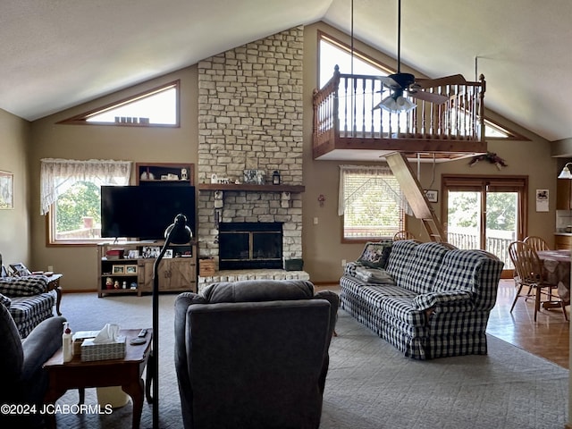 living area featuring carpet floors, a stone fireplace, a ceiling fan, and a healthy amount of sunlight