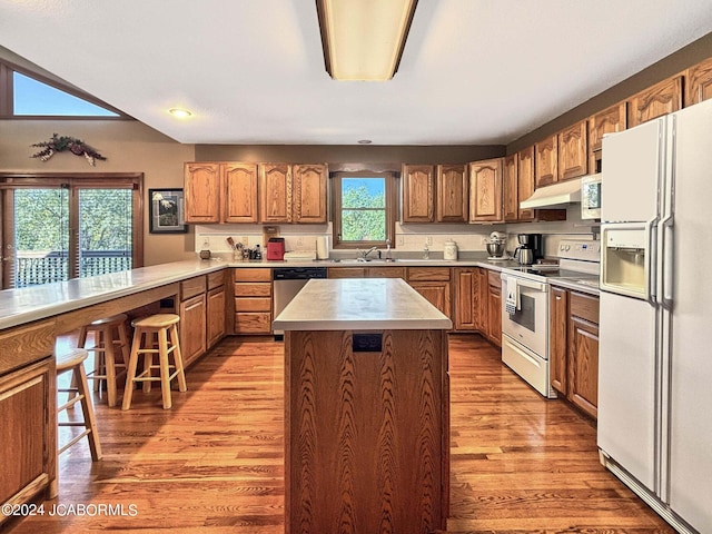 kitchen with white appliances, brown cabinetry, a breakfast bar area, a center island, and under cabinet range hood