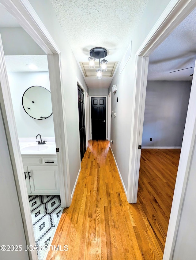 corridor with sink, light hardwood / wood-style floors, and a textured ceiling