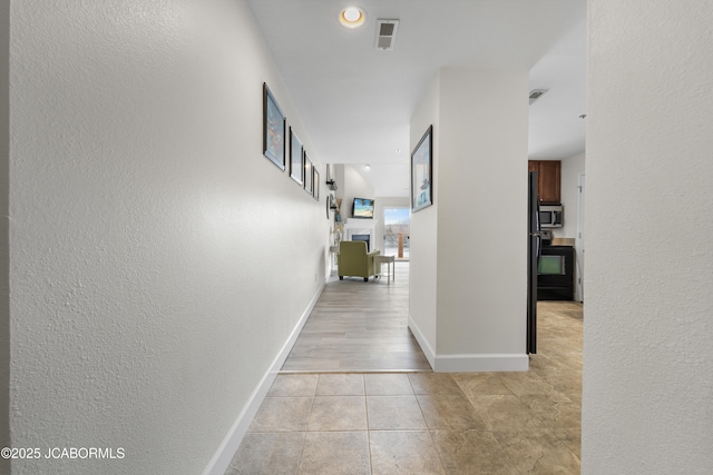 hall featuring visible vents, a textured wall, baseboards, and light tile patterned floors