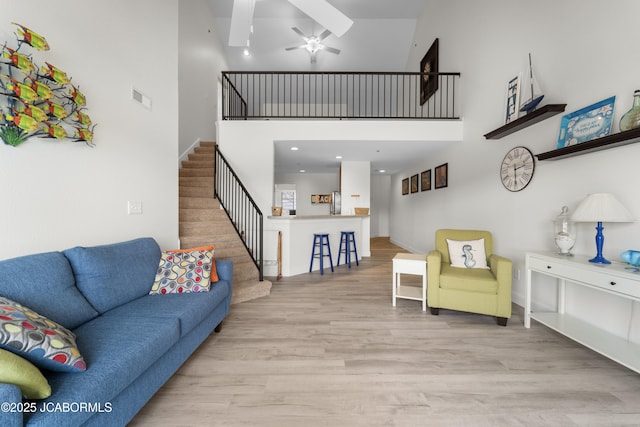 living room featuring a high ceiling, wood finished floors, visible vents, a ceiling fan, and stairs