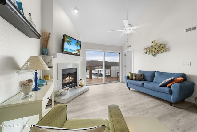 living area with ceiling fan, high vaulted ceiling, a fireplace, visible vents, and light wood-style floors