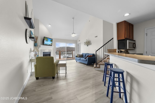 living area featuring high vaulted ceiling, a fireplace, baseboards, stairs, and light wood-style floors