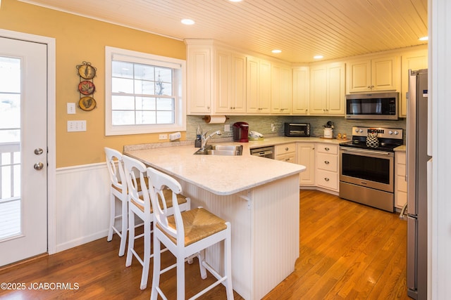 kitchen with appliances with stainless steel finishes, wood ceiling, wainscoting, a sink, and a peninsula