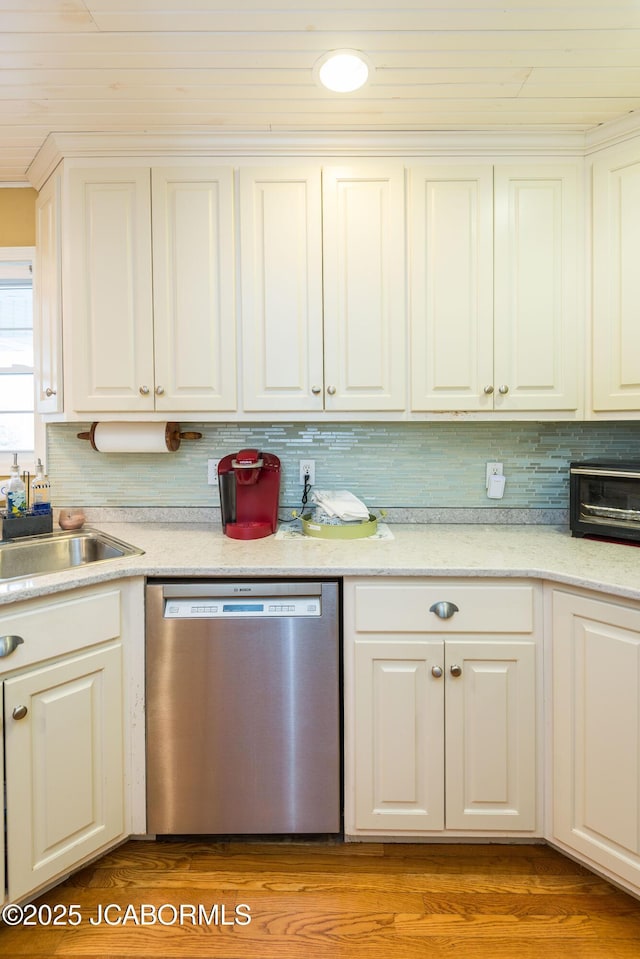 kitchen featuring light countertops, backsplash, stainless steel dishwasher, white cabinets, and a sink