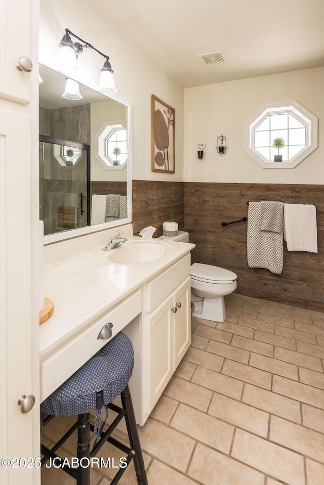 bathroom with toilet, vanity, visible vents, wainscoting, and a stall shower