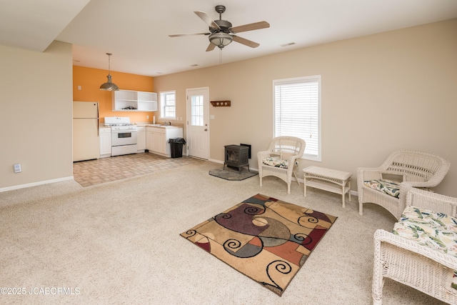 living room with a wood stove, light colored carpet, ceiling fan, and baseboards