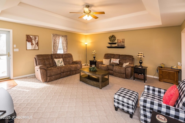 living room with light carpet, a tray ceiling, a ceiling fan, and baseboards