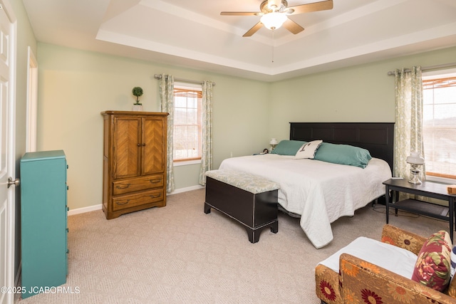 bedroom featuring a tray ceiling, multiple windows, and baseboards