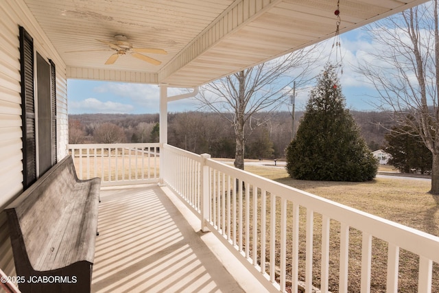 balcony featuring ceiling fan, a porch, and a wooded view