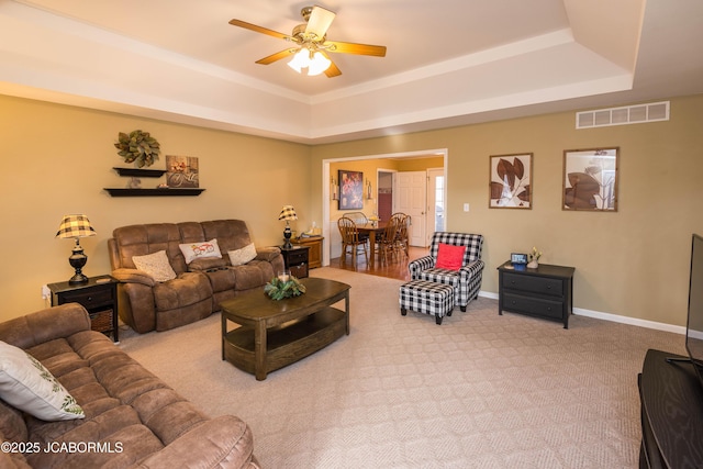 carpeted living room featuring a raised ceiling, visible vents, ceiling fan, and baseboards