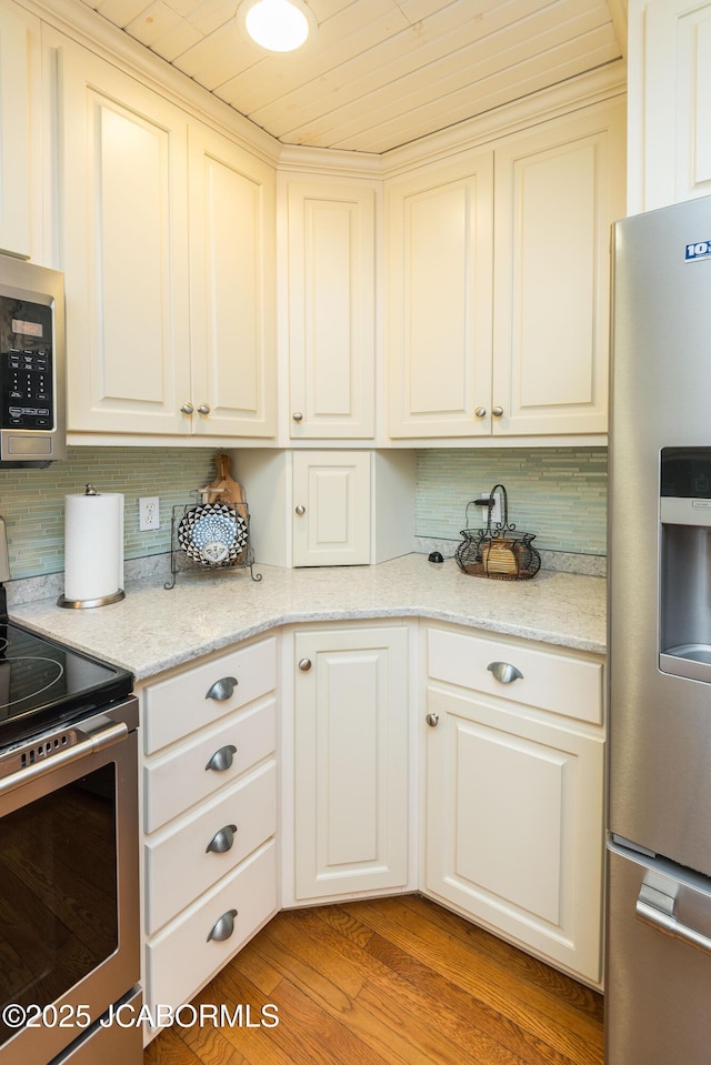 kitchen with light wood finished floors, appliances with stainless steel finishes, white cabinets, and backsplash